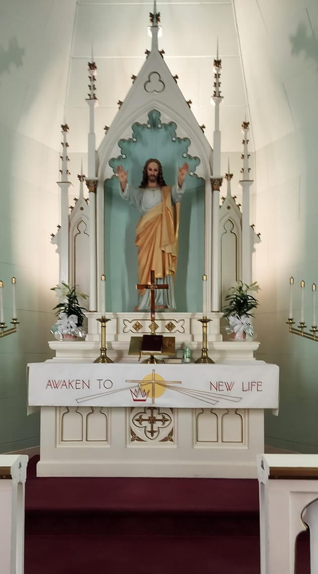 Altar at Immanuel Lutheran, Auroraville—Risen Christ statue, white reredos, candles, and “Awaken to New Life” paraments.